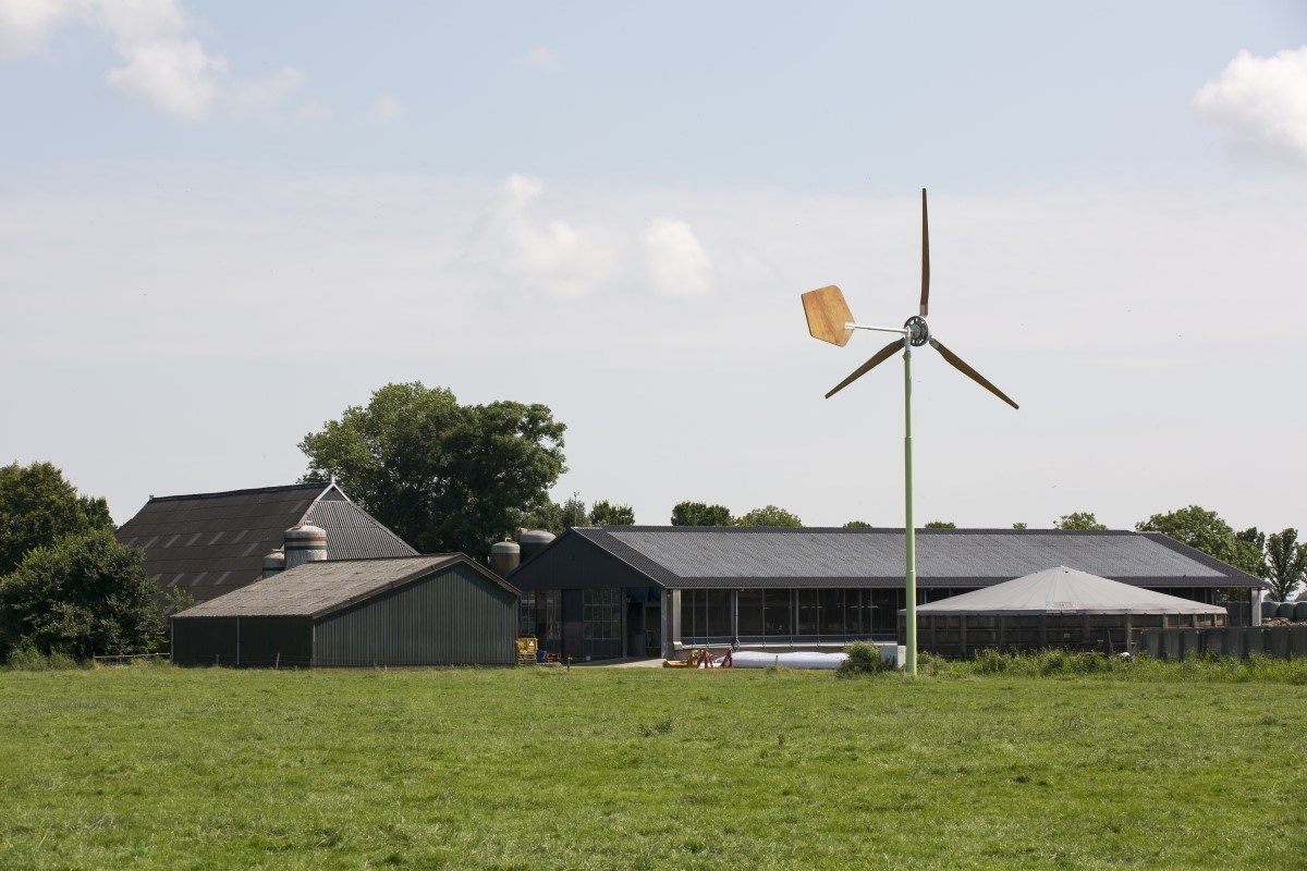 Foto van een boerderij met een kleine windmolen ervoor